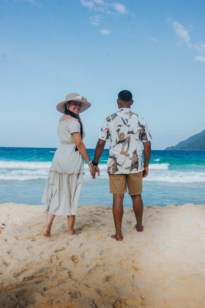 A couple enjoys a romantic walk on a beautiful Venezuelan beach, holding hands under a clear blue sky.